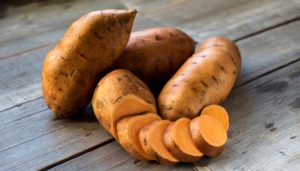 Raw sweet potatoes on wooden background closeup